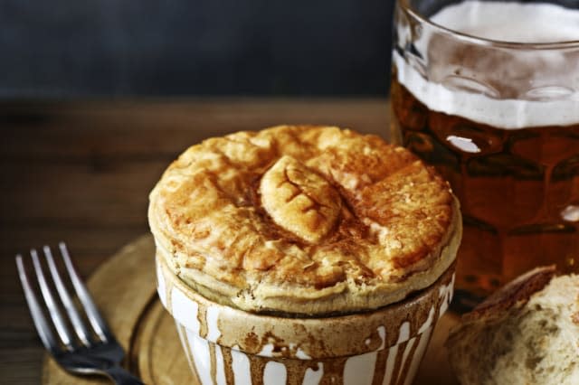 meat pie on bread board with pint of bitter