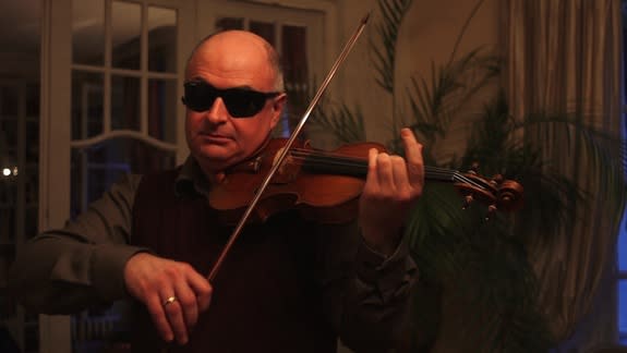 Soloist Ilya Kaler tests a violin. Kaler wears modified welder’s goggles to prevent him from seeing which instrument he is playing.