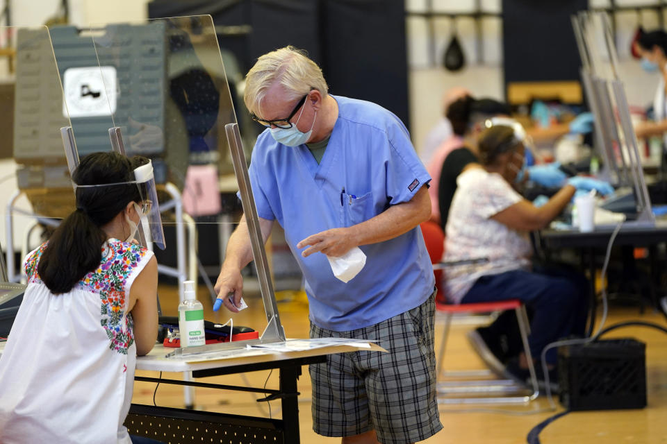 A voter, right, signs with a covered finger before voting Tuesday, July 14, 2020, in Houston. (AP Photo/David J. Phillip)