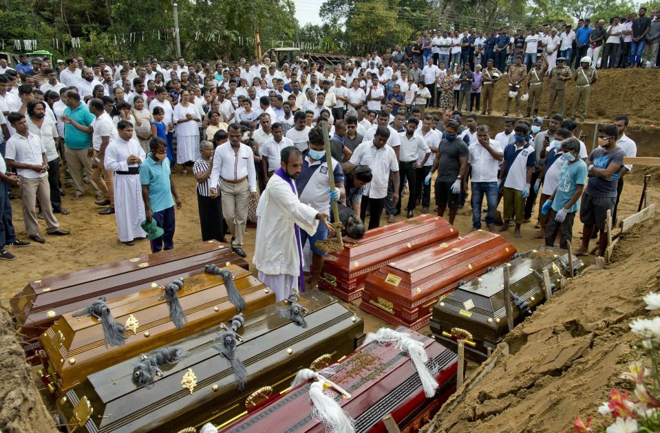 A priest conducts religious rituals during a mass burial for Easter Sunday bomb blast victims in Negombo, Sri Lanka, Wednesday, April 24, 2019. (AP Photo/Gemunu Amarasinghe)