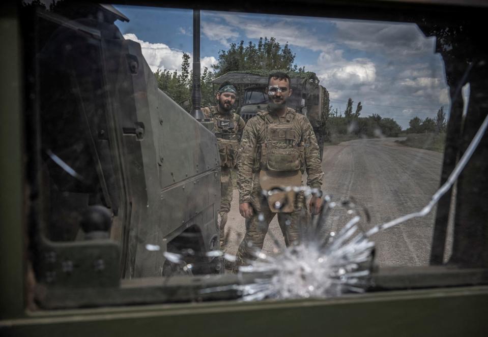 Ukrainian servicemen pose for a picture on a road in a photo taken through the smashed window of a military vehicle