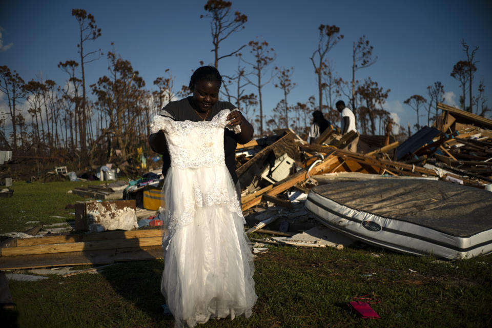 In this Sept. 8, 2019 photo, Synobia Reckley holds up the dress her niece wore as a flower girl at her wedding, as she goes through valuables in the rubble of her home destroyed one week ago by Hurricane Dorian in Rocky Creek East End, Grand Bahama, Bahamas. Synobia, 25, married two days after Hurricane Mathew in 2016, which passed over her home without doing serious damage. (AP Photo/Ramon Espinosa)