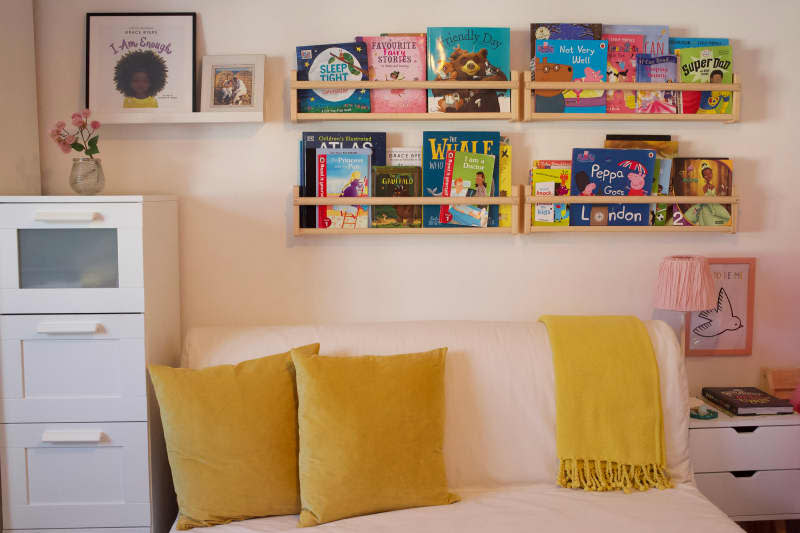 Decorative pillow and blanket top love seat in book filled child's room.