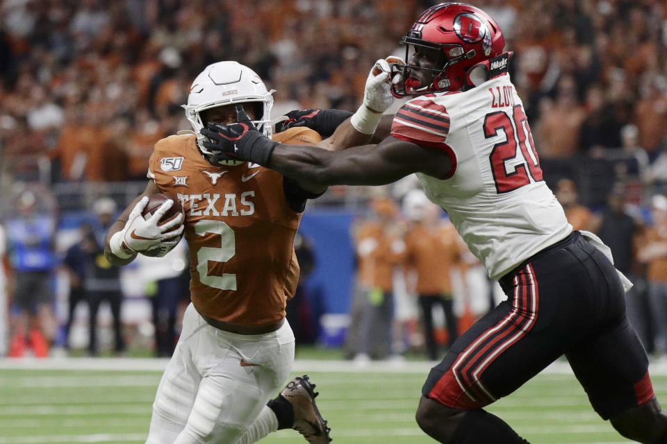 Texas running back Roschon Johnson (2) has his face mask grabbed by Utah linebacker Devin Lloyd (20) during the second half of the Alamo Bowl NCAA college football game in San Antonio, Tuesday, Dec. 31, 2019. (AP Photo/Eric Gay)