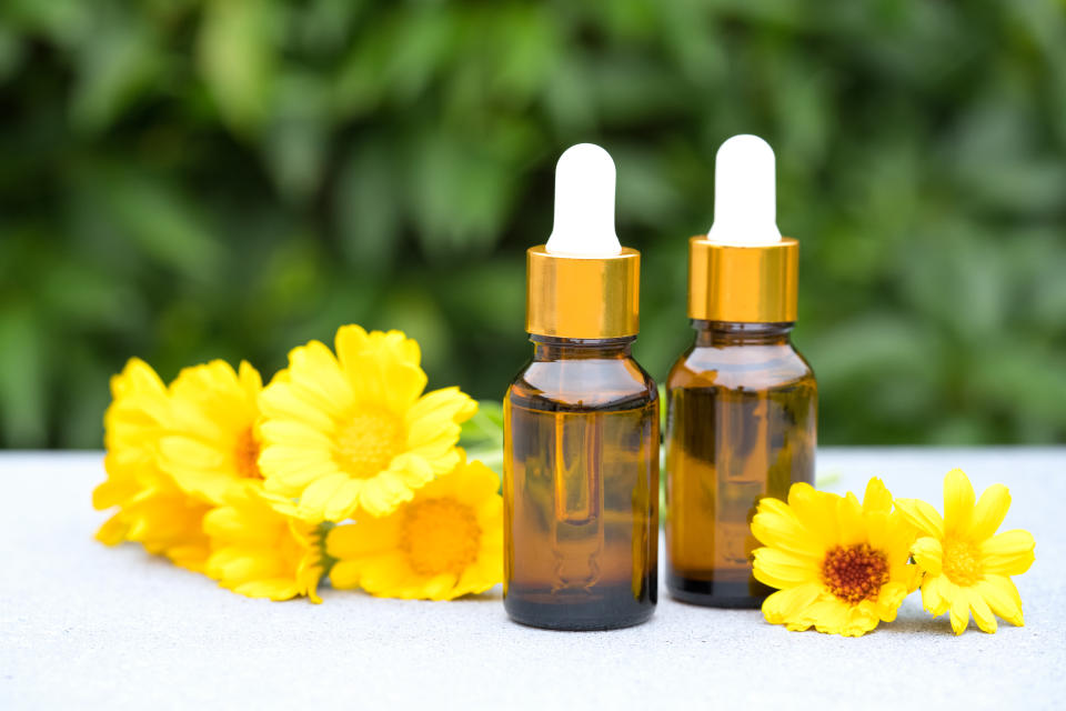 Bottles of calendula oil on a table and surrounded by calendula flowers