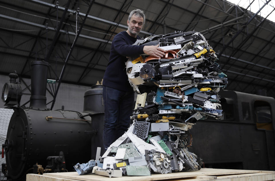 In this picture taken on Thursday, April 11, 2019, designer Piet Hein Eek poses next to his creation 'Electronic Man', made with recycled plastic pieces of variuos electronic devices, during the 'RO Master's Pieces exhibition', on the sidelines of the Salone del Mobile International Furniture Fair week, in Milan, Italy. Scientists and environmental activists have been long raised the alarm on plastic pollution. Now, the high-end design world is getting in on the growing global effort to tackle plastic pollution -- by upcycling discarded objects into desirable one-off design pieces. (AP Photo/Luca Bruno)