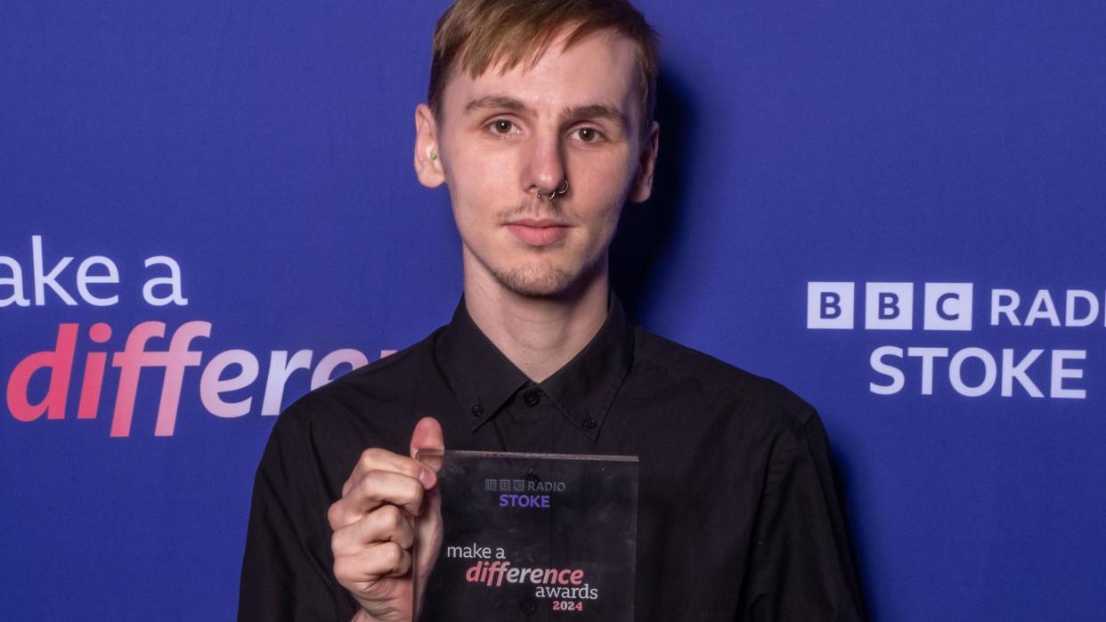 A man wearing a black shirt holds an award as he poses for a photo