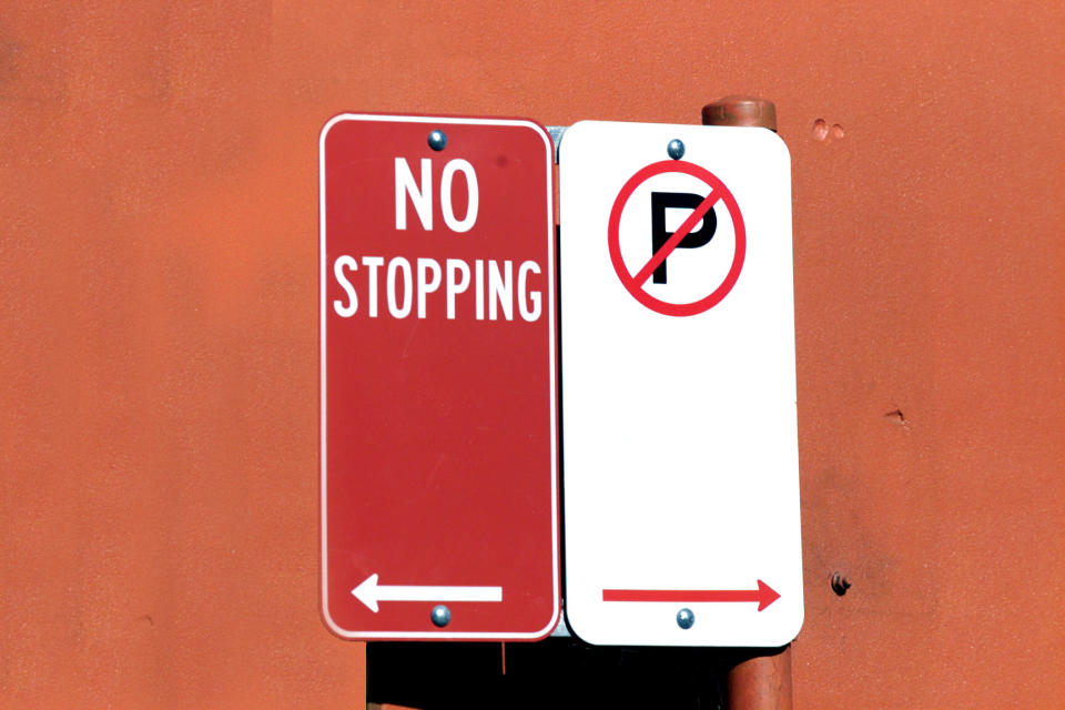 Pictured is a no stopping sign and a no parking sign in front of an orange wall. 