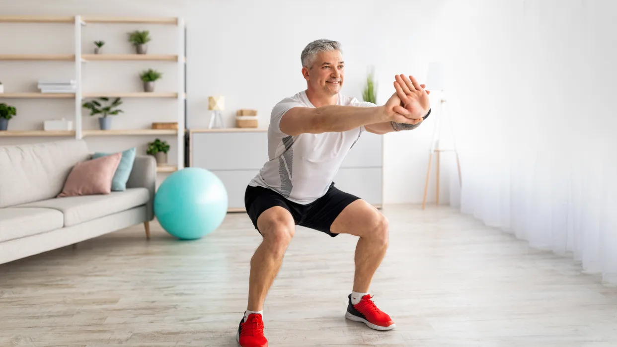 A man performing a squat at home as part of a joint strengthening routine .