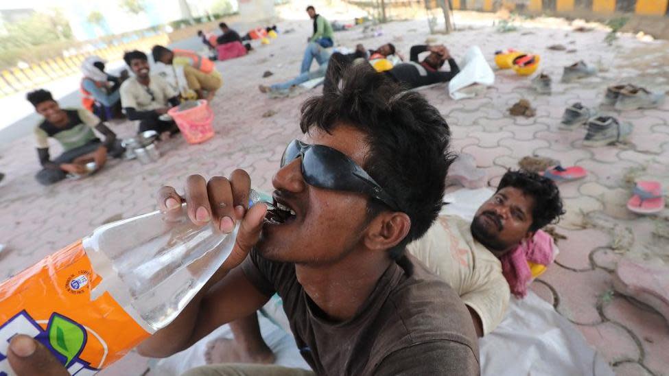 An Indian worker drinks water from a bottle while others rest on the pavement in the shadow of an overpass on a hot day near New Delhi, India, 18 June 2024. 