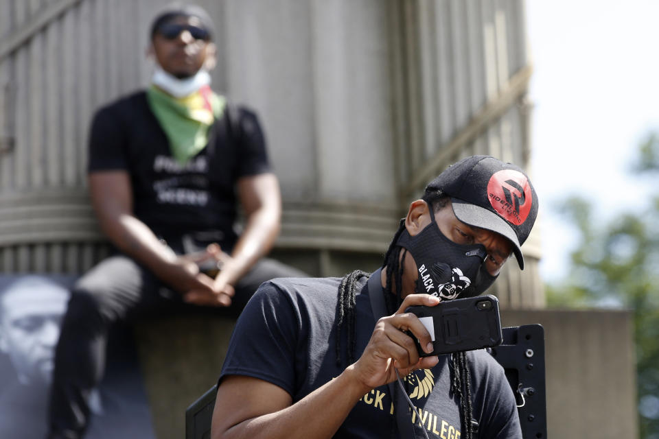 A man uses his cell phone to record speakers as another listens from the pedestal of a column during a Caribbean-led Black Lives Matter rally at Brooklyn's Grand Army Plaza, Sunday, June 14, 2020, in New York. (AP Photo/Kathy Willens)