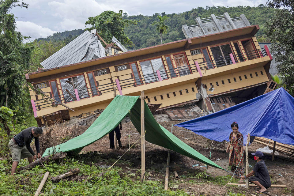 Residents build tents outside their house badly damaged by earthquake in Mamuju, West Sulawesi, Indonesia, Tuesday, Jan. 19, 2021. Aid was reaching the thousands of people left homeless and struggling after an earthquake that killed a number of people struck early Friday. (AP Photo/Yusuf Wahil)