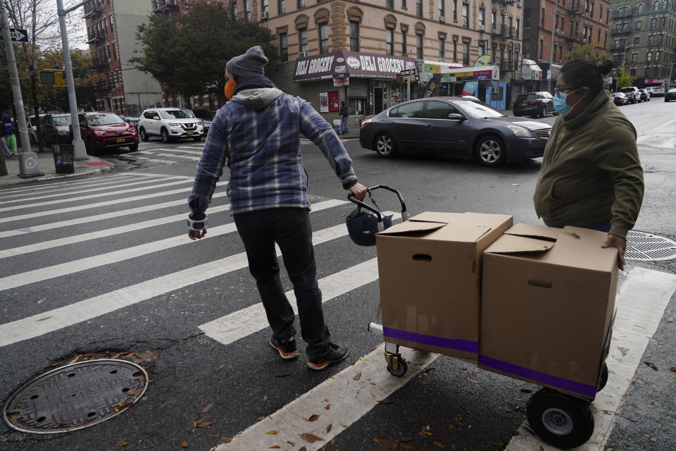 Yahaira Saavedra, right, co-owner of the Mexican restaurant La Morada, and volunteer Dan Zimberg, left, cross a street pushing a trolley load of boxed meals prepared at the South Bronx restaurant, Wednesday Oct. 28, 2020, in New York. After a fund raising campaign during the coronavirus pandemic, Saavedra and her parents transformed the restaurant into a soup kitchen, serving 650 meals daily. (AP Photo/Bebeto Matthews)