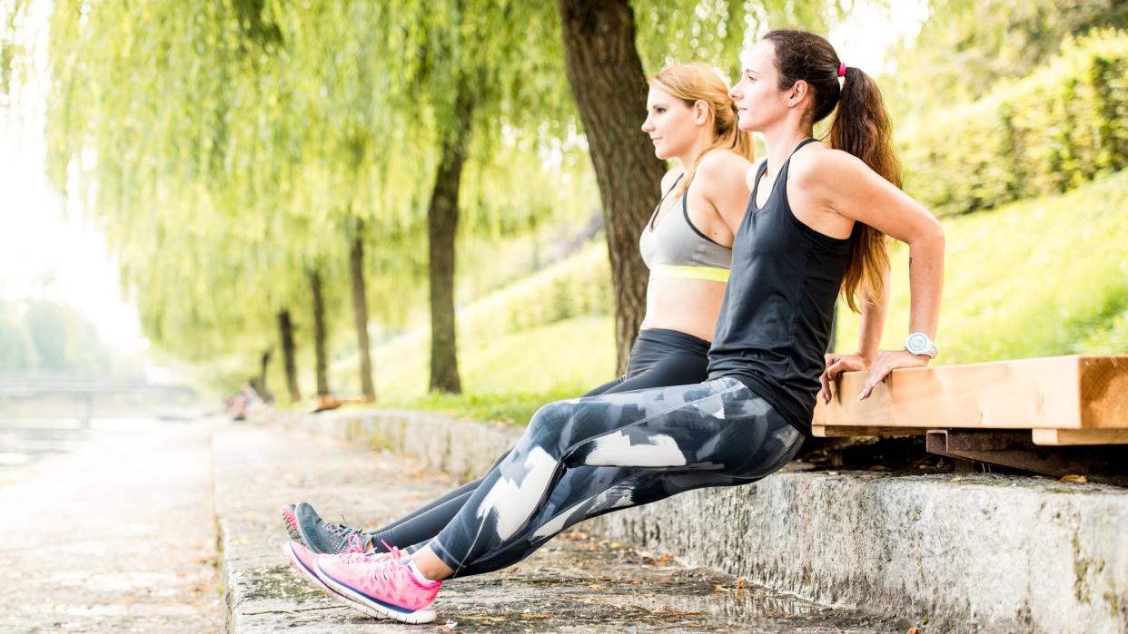  Two women doing triceps dips outdoors. 