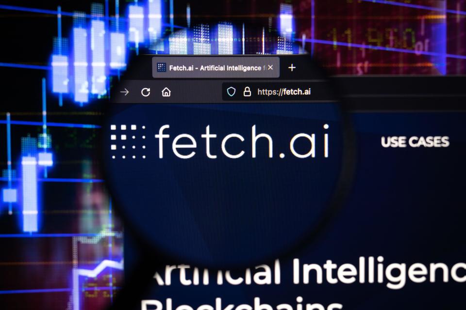 Fetch.ai company logo on a website, seen on a computer screen through a magnifying glass. AI tokens, such as fetch.ai, gained on Thursday. 