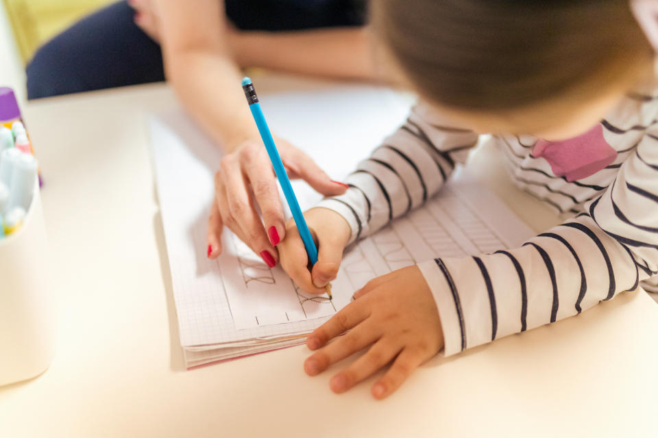 A teacher helps a student write out letters on a worksheet