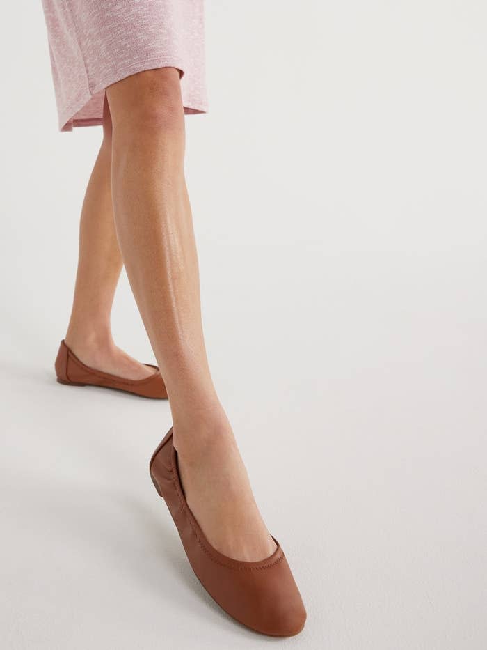 Close-up of a person's lower legs wearing flat brown shoes, dressed in a pink skirt