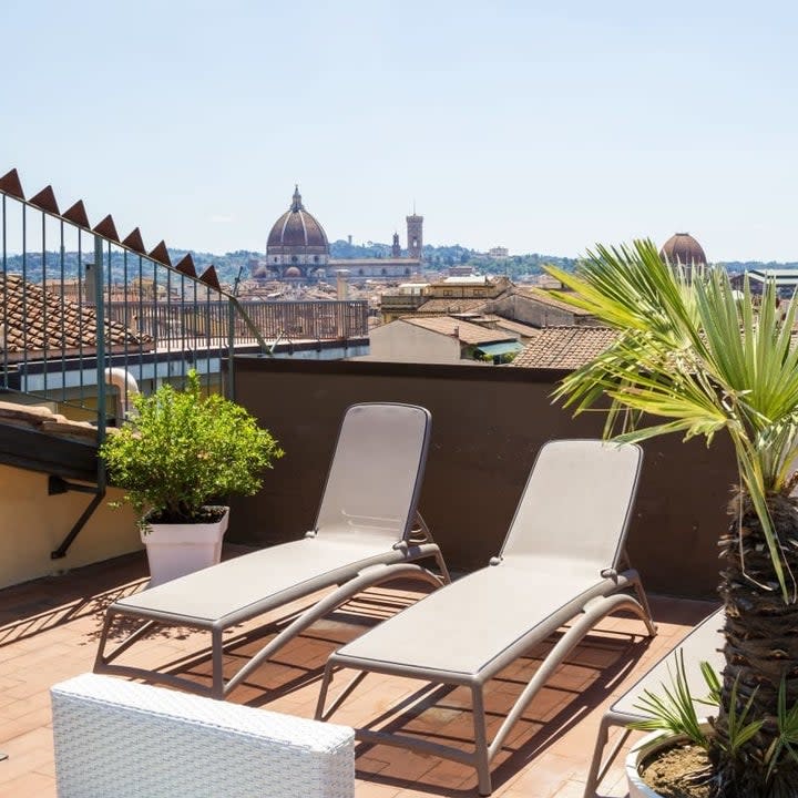 Rooftop terrace with plants and lounge chairs overlooking the city of Florence