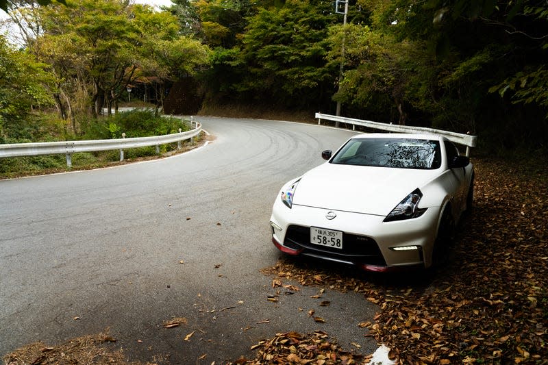 a white nissan fairlady z nismo parked at the edge of a winding mountain road in autumn in japan