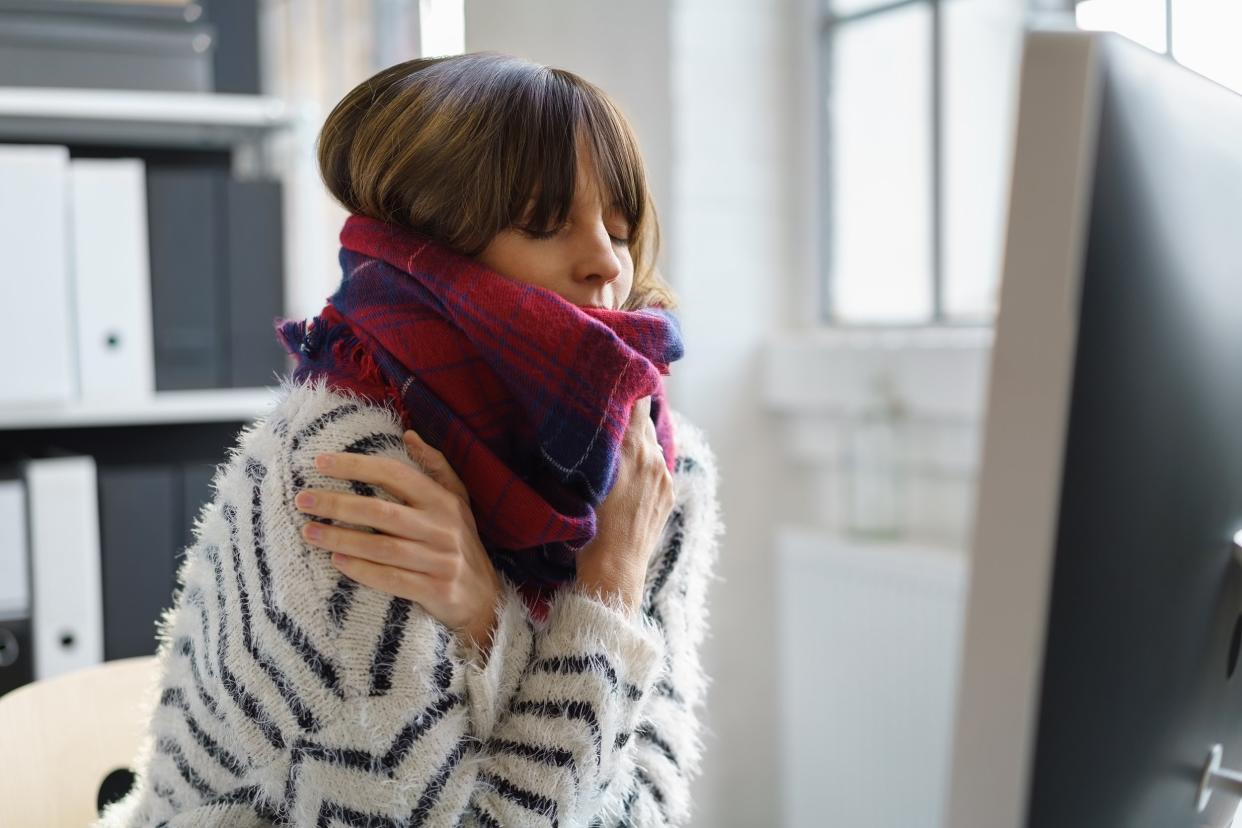 sick woman shivering in the office wrapped in a thick woolly winter scarf