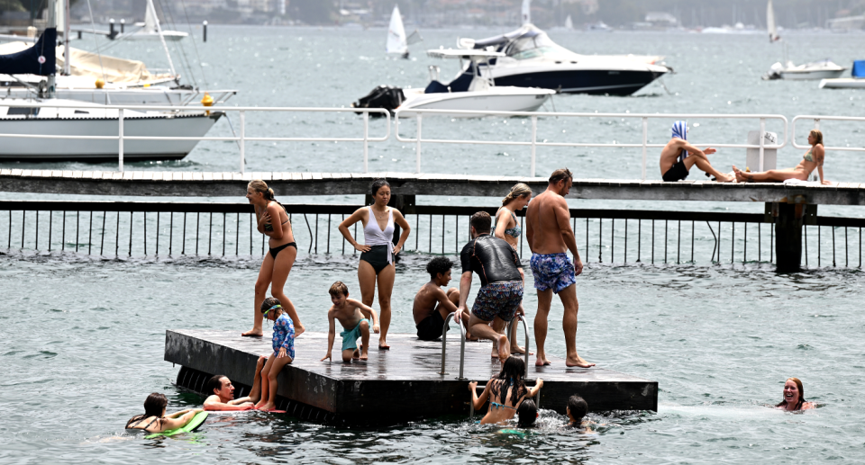 Aussies swimming in water while many stand on a jetty in the sunshine. 