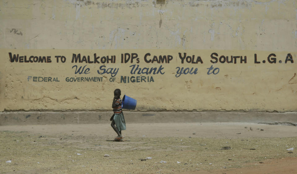 In this photo taken on Thursday, Feb. 21, 2019, a child displaced by Islamist extremists walks past a welcome sign to Malkohi camp in Yola, Nigeria. For those who live in the makeshift camp for Nigerians who have fled Boko Haram violence, the upcoming presidential vote isn’t a topic of conversation, because nearly all are more worried about putting food on the table.(AP Photo/ Sunday Alamba)