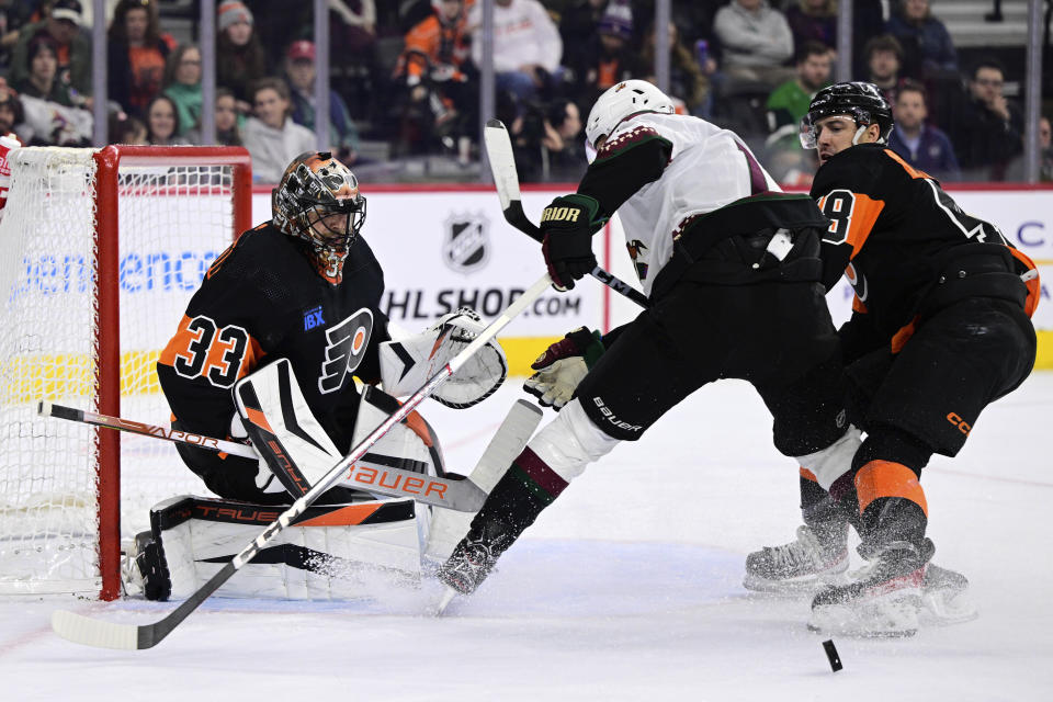 Philadelphia Flyers goaltender Samuel Ersson, left, looks for the puck after making a save past teammate Morgan Frost, right, and Arizona Coyotes' Nick Bjugstad, center, during the first period of an NHL hockey game, Monday, Feb. 12, 2024, in Philadelphia. (AP Photo/Derik Hamilton)