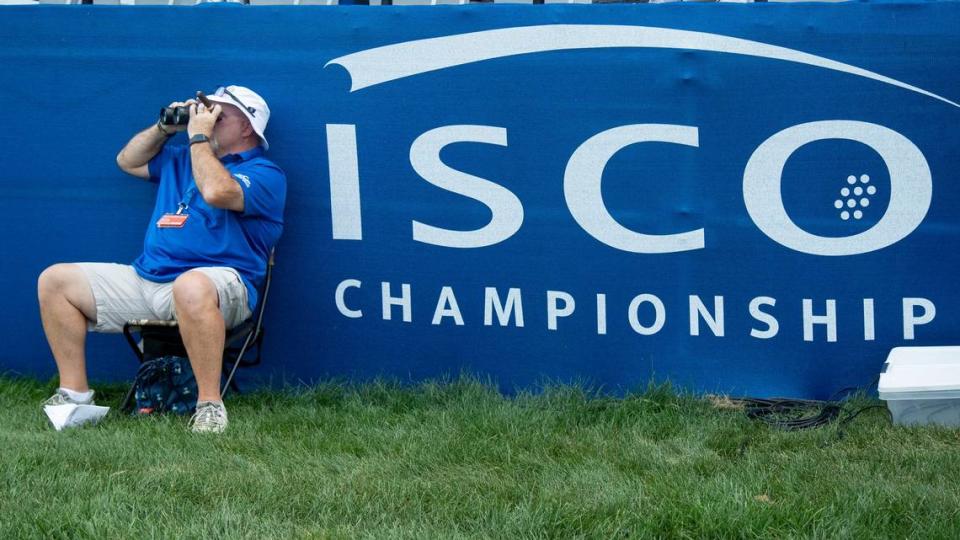 A volunteer uses binoculars to look at other golfers across a lake during the first round of the 2024 ISCO Championship at Champions at Keene Trace Golf Club in Nicholasville, Ky, on Thursday, July 11, 2024. 