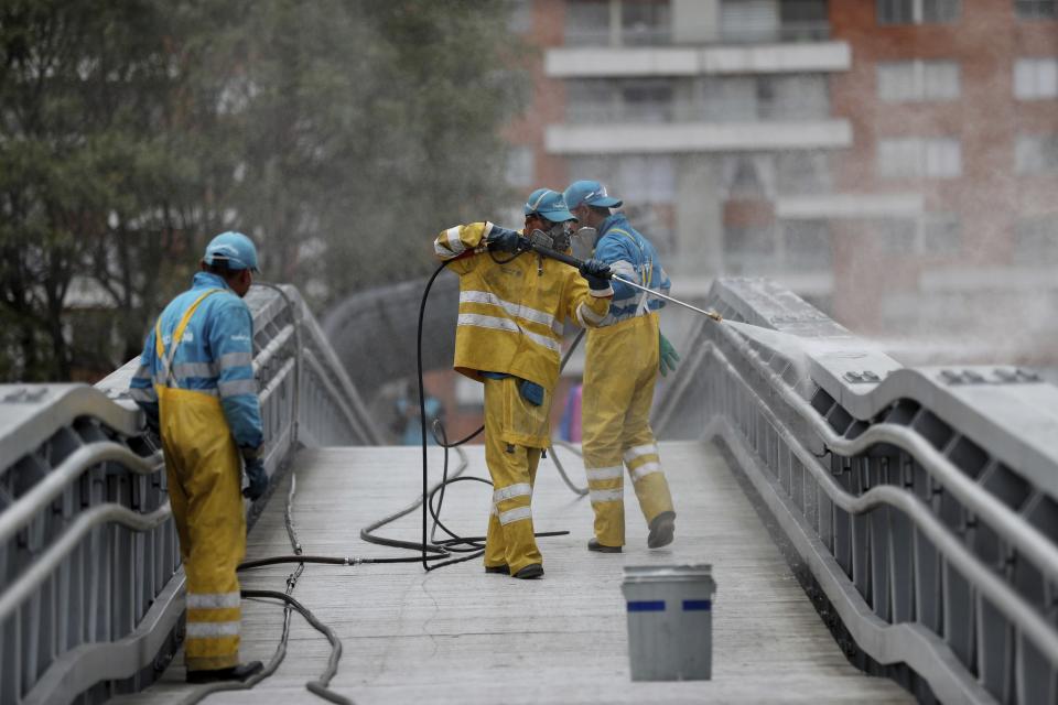 Varios trabajadores limpian un puente peatonal para tratar de reducir la propagación del coronavirus, en Bogotá, Colombia, el jueves 30 de abril de 2020. (AP Foto/Fernando Vergara)