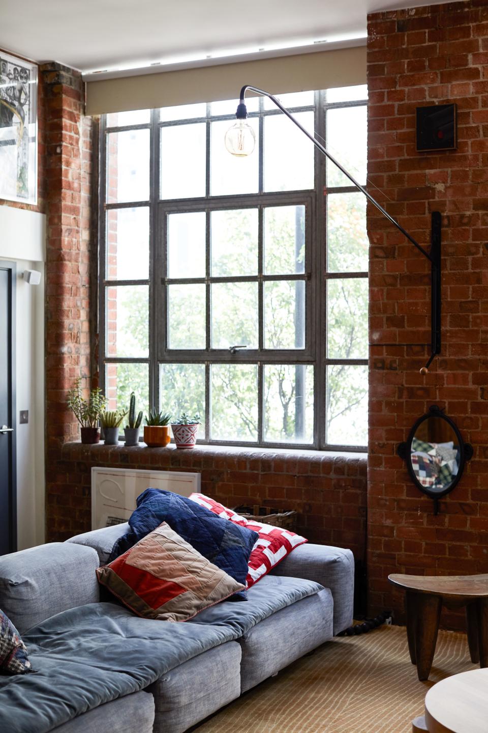 Tovey loves the way the exposed-brick metal framed windows nod to the buildings industrial past as a warehouse. In a corner of the living area, the modular sofa, a Matthew Hilton design for SCP, is heaped with cushions from French fashion label APC; each one is made from recycled clothes from the previous year’s collections. Below the Jean Prouvé wall light hangs a mirror by Swiss artist Nicolas Party, with a piece by Emily Furr above. A collection of succulents, displayed in vintage planters, enjoys a sunny spot on the windowsill. Works by Torey Thornton (under planters) and Oscar Murillo (over utility door).