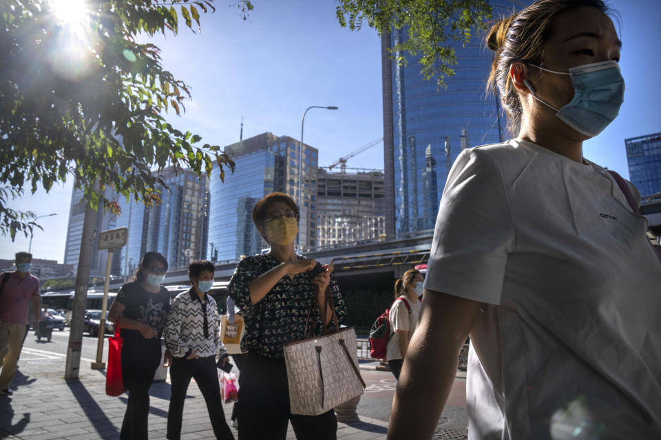 Commuters wearing face masks walk along a street in the central business district in Beijing, Thursday, Sept. 1, 2022. (AP Photo/Mark Schiefelbein)