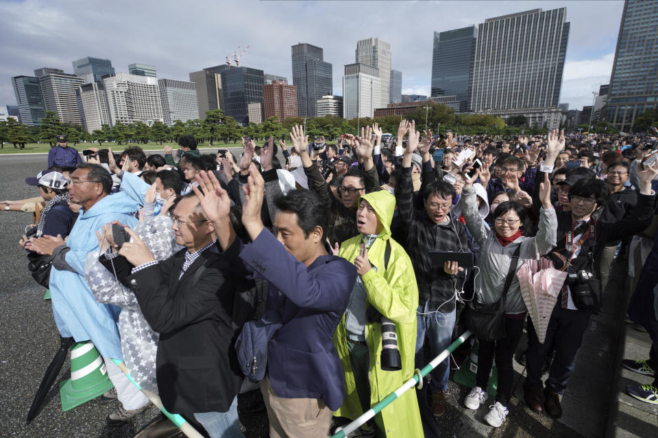 People outside of the Tokyo Imperial Palace follow Prime Minister Shinzo Abe's three "banzai" cheers for the 59-year-old Emperor Naruhito during the enthronement ceremony, Tuesday, Oct. 22, 2019, in Tokyo, Japan. (AP Photo/Eugene Hoshiko)