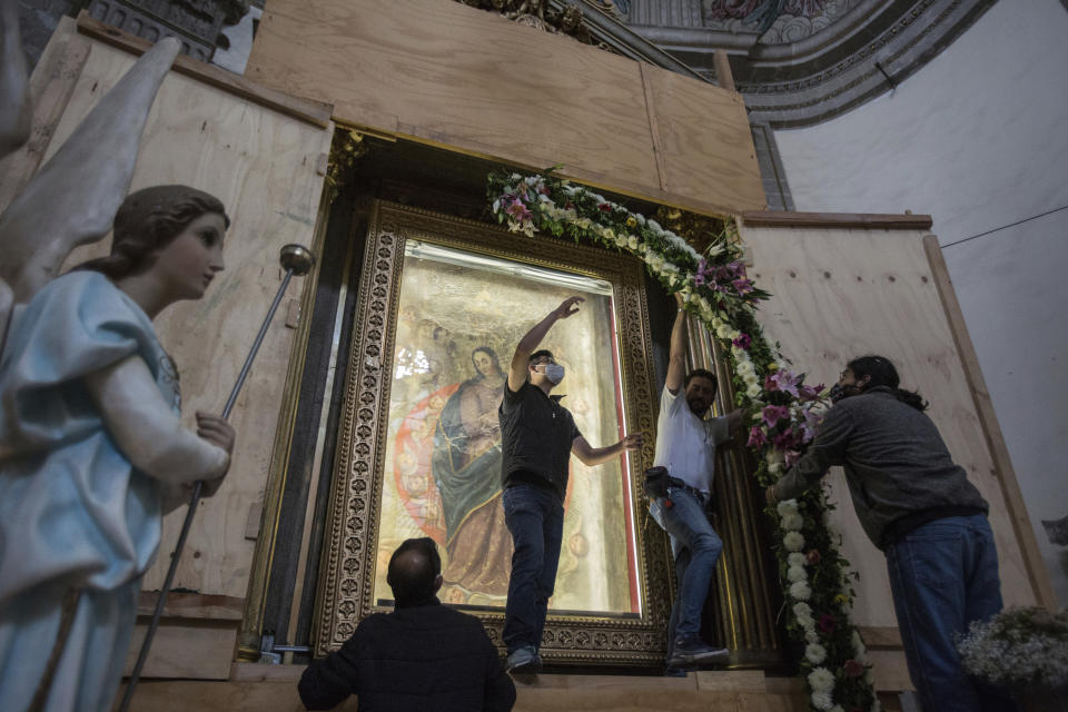 Parishioners remove a portion of a flower arch surrounding a painted copy portraying the Assumption of the Virgin inside the quake-damaged Our Lady of the Angels Catholic church, in Mexico City, Sunday, Aug. 7, 2022. During restoration efforts the image is boxed off in a protective framework and covered by glass and wood panels that open and close like a book. (AP Photo/Ginnette Riquelme)