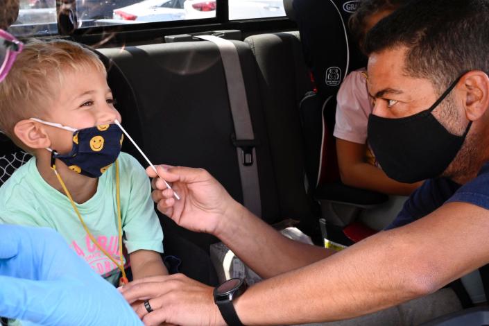 4 year old smiling in car seat, as dad performs nose swab on him for a rapid test