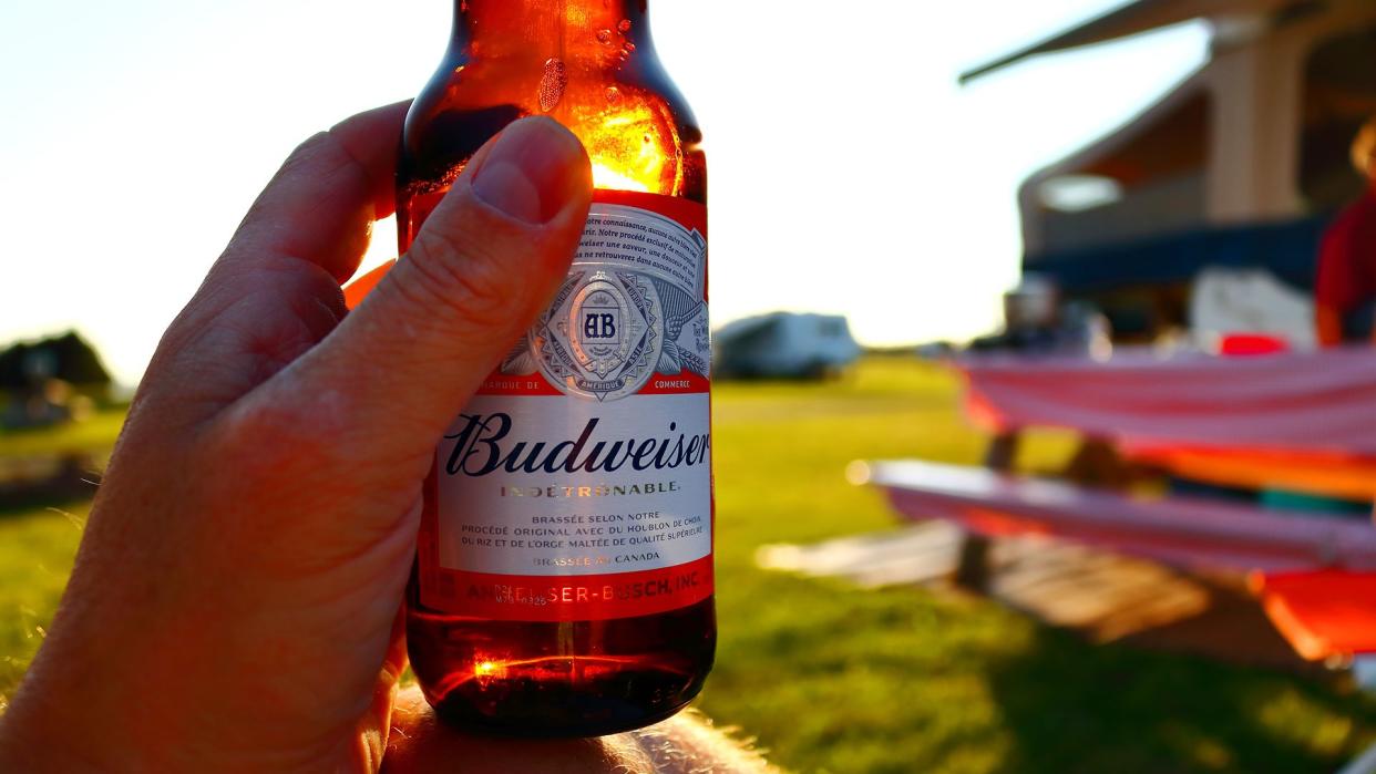 A person sitting at a campsite enjoying a Budweiser beer as the sun sets and the light highlights the bottle.