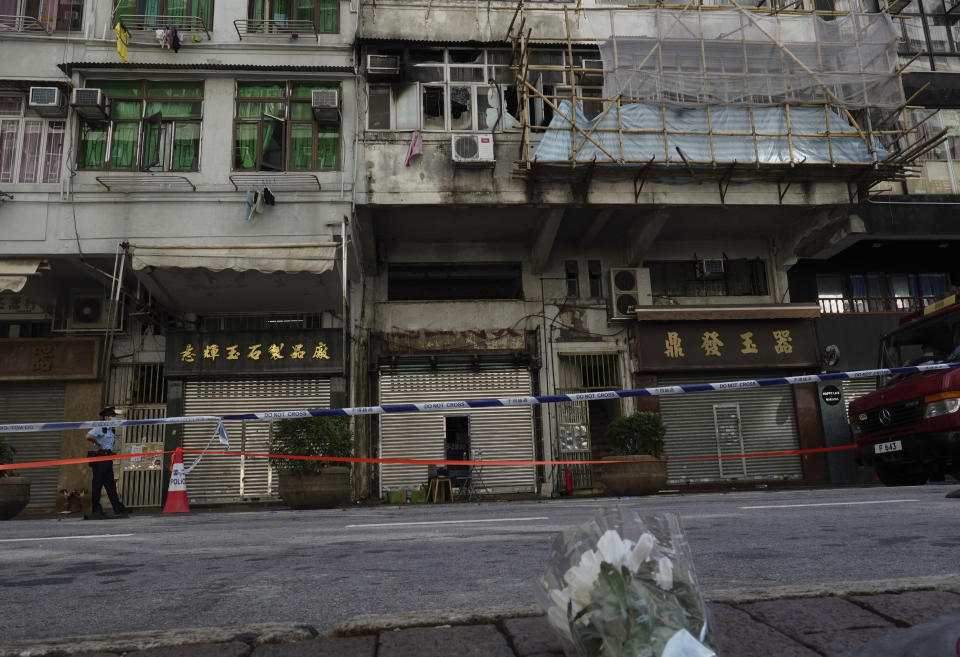 Flowers are placed at a fire site, top center with broken windows, in Hong Kong Monday, Nov. 16, 2020. City authorities said a fire in a crowded residential district in Hong Kong has "caused a number of deaths and injuries". (AP Photo/Vincent Yu)