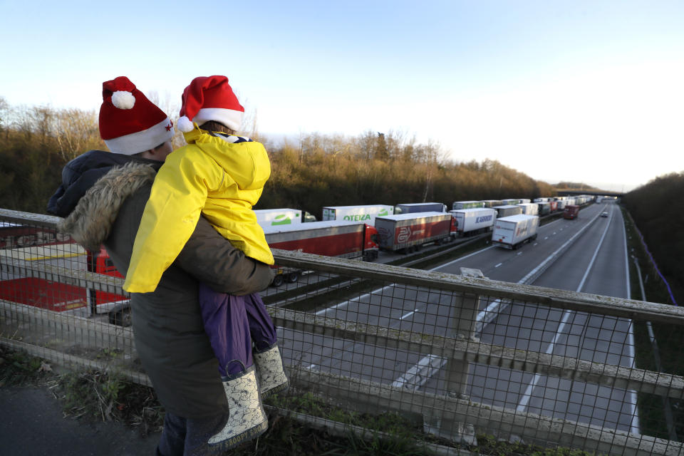 A mother and child look at the line of trucks parked up on the M20, part of Operation Stack in Ashford, Kent, England, Friday, Dec. 25, 2020. Thousands wait to resume their journey across The Channel after the borders with France reopened. Trucks inched slowly past checkpoints in Dover and headed across the Channel to Calais on Thursday after France partially reopened its borders following a scare over a rapidly spreading new virus variant. (AP Photo/Kirsty Wigglesworth)