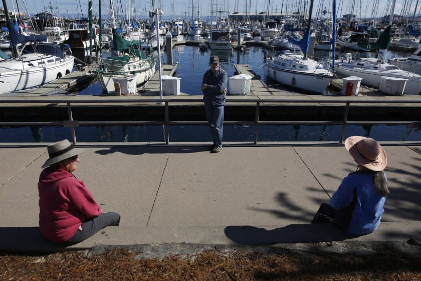 In this photo taken Tuesday April 7, 2020, area residents Terry Hanna, left, her husband, Mike, center, and Melanie Cervi, right, practice social distancing near Fisherman's Wharf in Monterey, Calif., Tuesday, April 7, 2020.