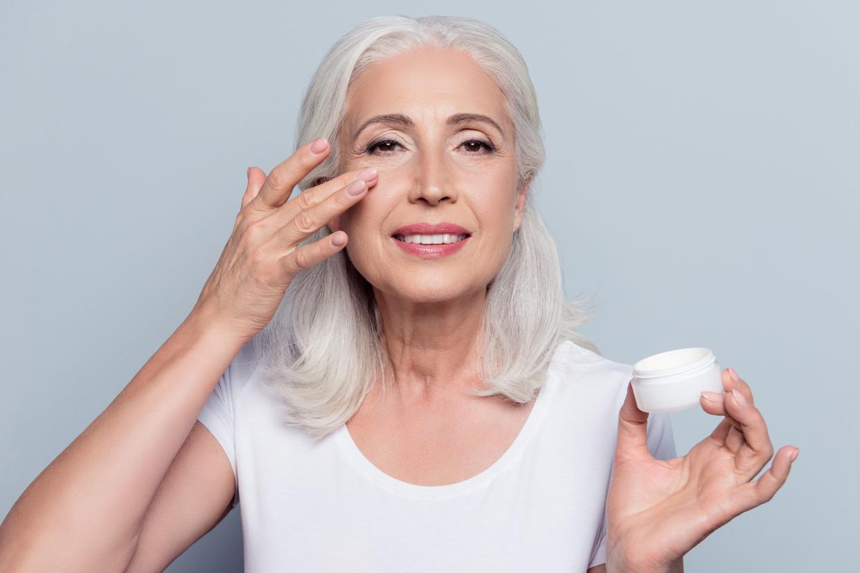 woman applying eye cream holding jar of cosmetic product