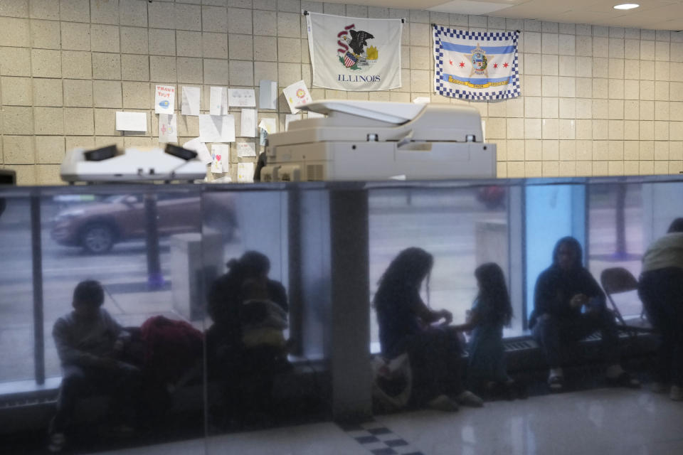 Immigrants from Venezuela are reflected in a marble wall while taking shelter at the Chicago Police Department's 16th District station on Monday, May 1, 2023. Chicago has seen the number of new arrivals grow tenfold in recent days. Shelter space is scarce and migrants awaiting a bed are sleeping on floors in police stations and airports. (AP Photo/Charles Rex Arbogast)