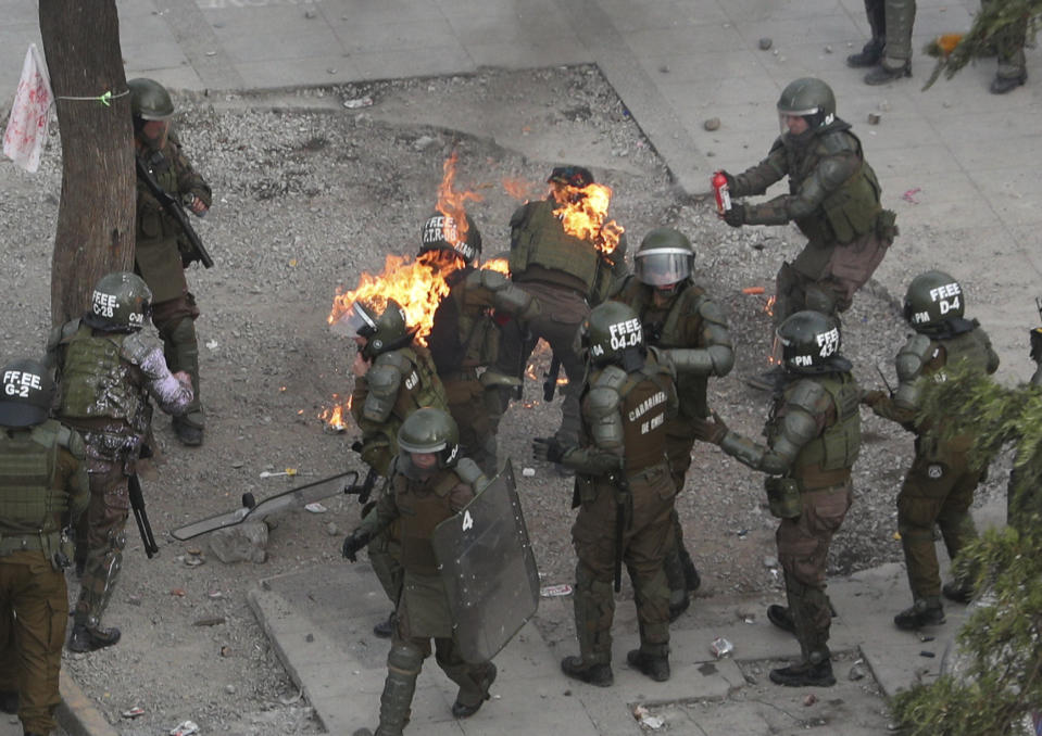 Police scramble after being hit with a gasoline bomb thrown by protesters during an anti-government protest in Santiago, Chile, Monday, Nov. 4, 2019. Chile has been facing weeks of unrest, triggered by a relatively minor increase in subway fares. The protests have shaken a nation noted for economic stability over the past decades, which has seen steadily declining poverty despite persistent high rates of inequality. (AP Photo/Esteban Felix)