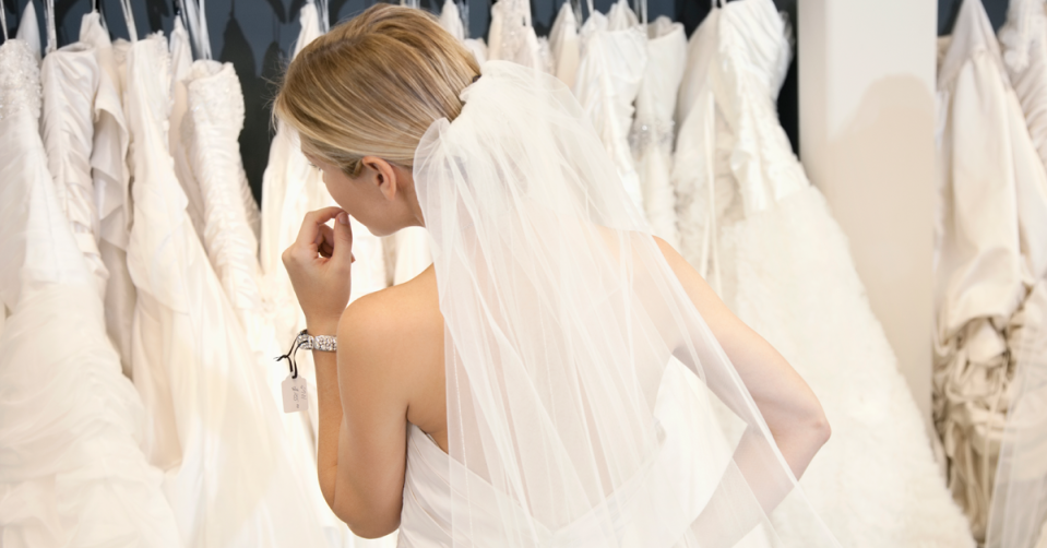 A bride looks at wedding dresses on a rack. 