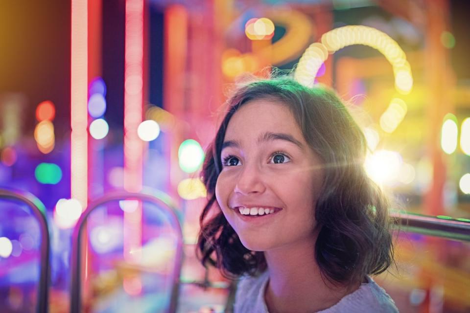 A child smiles with blurred bright lights in the background to indicate an amusement park setting.