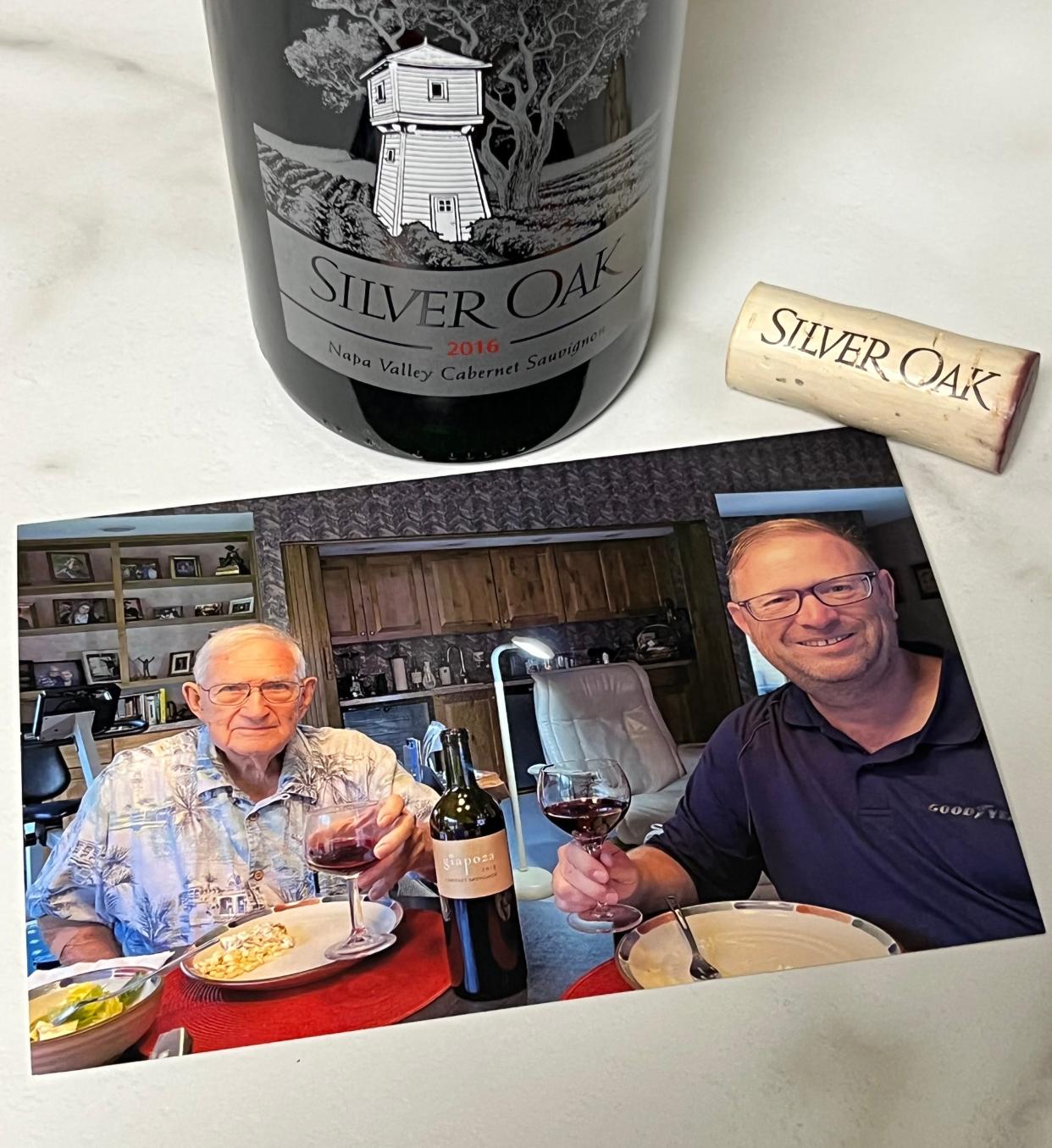 A photo of George Kirk and his son Rich Kirk enjoying a recent dinner and a glass of wine. The photo sits next to an opened bottle of Silver Oak cabernet they never got to enjoy together.