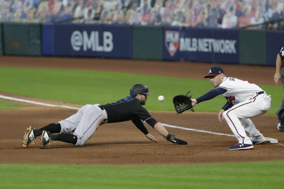 Miami Marlins' Jon Berti dives back to first base as Atlanta Braves first baseman Freddie Freeman attempt to tag him out during the eighth inning in Game 2 of a baseball National League Division Series Wednesday, Oct. 7, 2020, in Houston. (AP Photo/Michael Wyke)