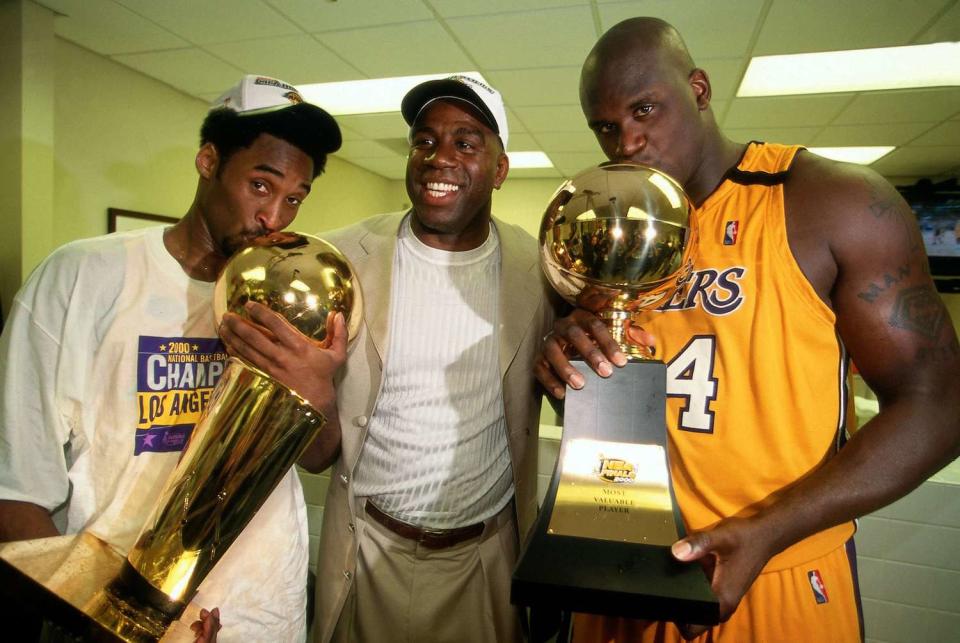 Shaquille O'Neal #34 and Kobe Bryant of the Los Angeles Lakers pose with Lakers legend Magic Johnson after winning the NBA Championship trophy after defeating the Indiana Pacers in Game Six of the 2000 NBA Finals on June 19, 2000 at Staples Center in Los Angeles, California.