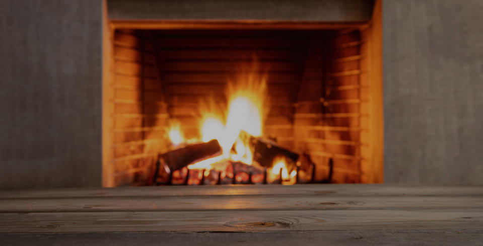 Table on blur burning fireplace background. Empty wooden planks, space for advertise. Winter holidays cozy warm home, Christmas, New Year template.