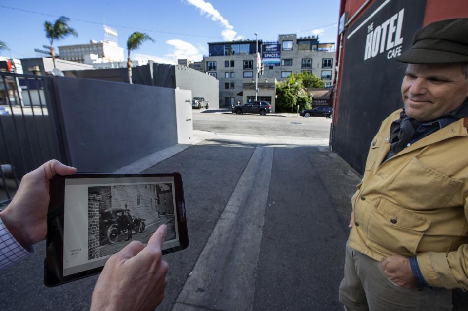 A man looks at an iPad held by another man pointing to a scene from a movie on the screen