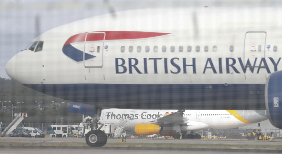 Seen though a perimeter fence a British Airways aircraft takes off past a Thomas Cook plane in the background at Gatwick Airport, England, Monday, Sept. 23, 2019. British tour company Thomas Cook collapsed early Monday after failing to secure emergency funding, leaving tens of thousands of vacationers stranded abroad. (AP Photo/Alastair Grant)