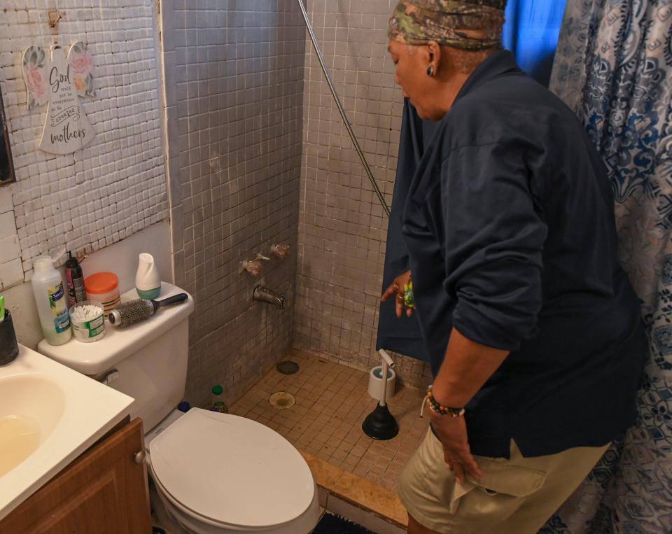 Bonnie Cooke points out the drain in her bathroom shower in which the plumbing backs up and needs to be manually pumped out with a plunger. Cooke and her attorney believes the septic backup may have caused by damaged a drain pipe from her septic tank field caused by the retention pond created behind her home.